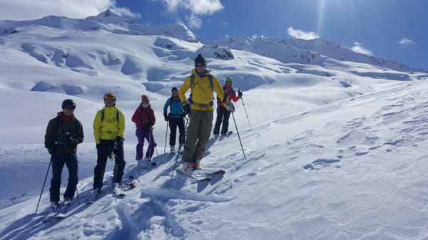Skitourengeher:innen während einer Pause bei Sonnenschein und frisch eingeschneiter Berglandschaft