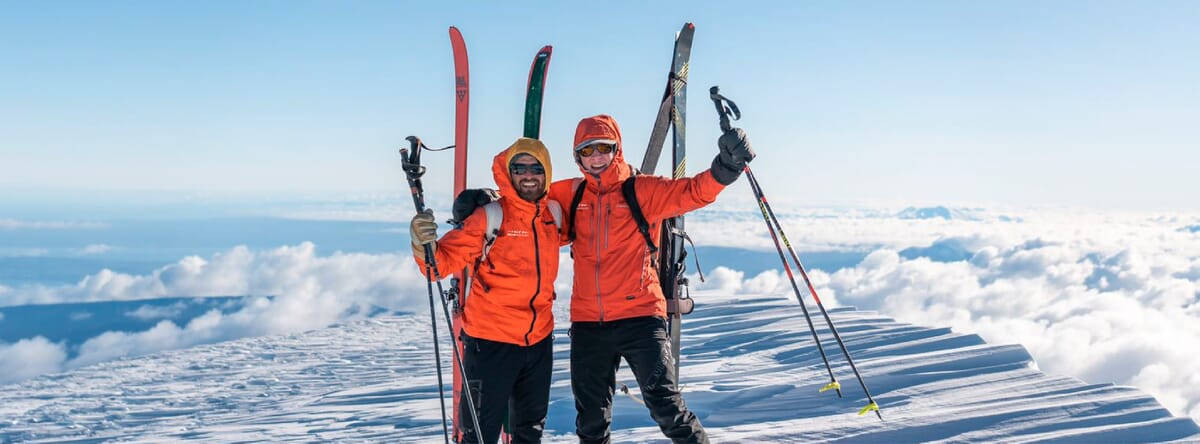 Skitourengeher in Chile auf einem Gipfel mit Skis aufgebunden und roter Jacke