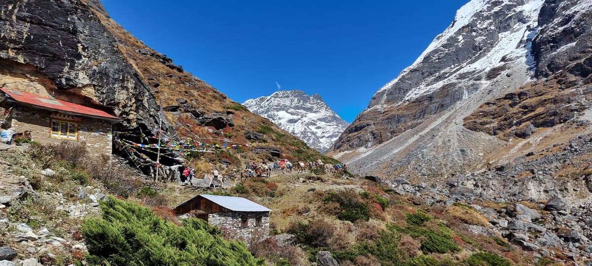 Mera Peak Trekking | Gruppe im Aufstieg, Mera Peak im Hintergrund, einfache Häuser im Vordergrund