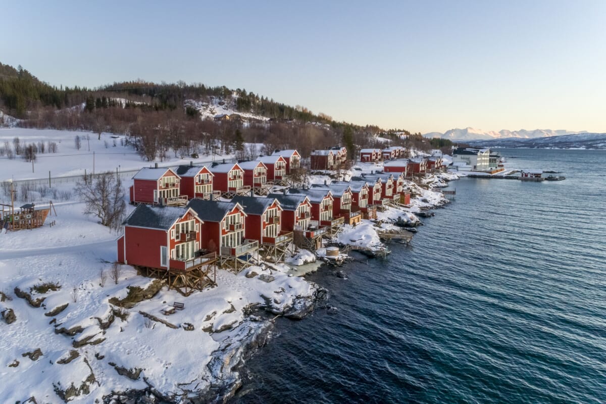 Traditionelle Rorbuer Fischerhütten in Nordnorwegen, blaues Meer, Schnee und Berge im Hintergrund