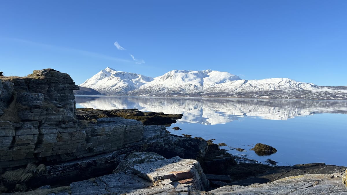 Naturaufnahme, im Vordergrund Felsen und das Meer und hinten weisse Berge