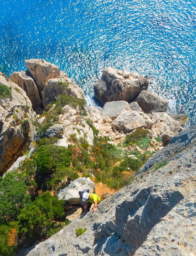 Ein Kletterer im Vorstieg, scharfer Kalkfels, im Hintergrund das Meer, Klettern im Süden