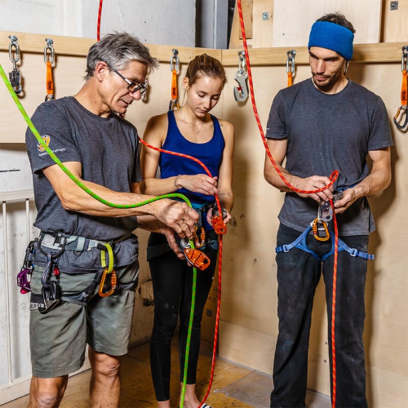 Drei Personen beim Seilhandling, Kletterhallte, Kletterseile und Sicherungsgerät.