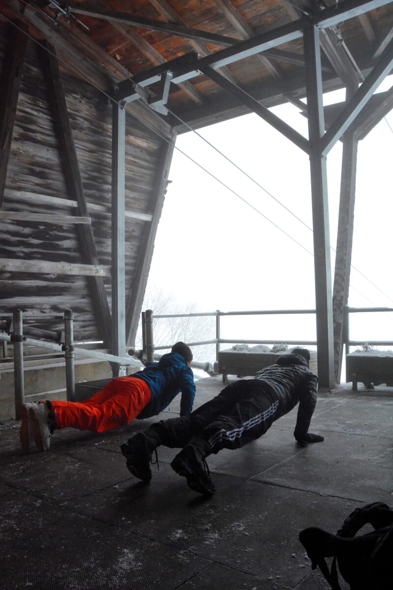Zwei Personen sind am Übungen machen bei der Bergstation, hinten Nebel