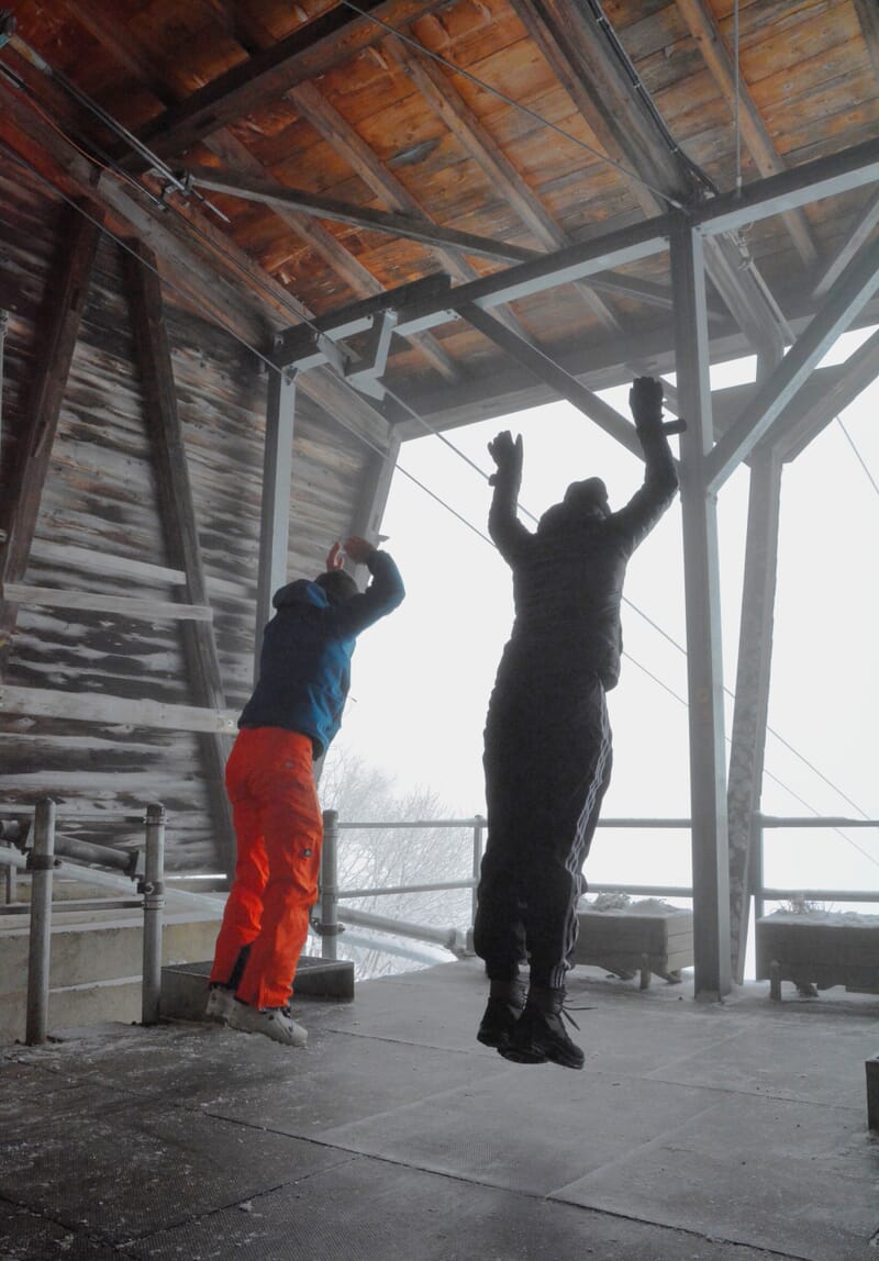 Zwei Personen sind am Aufspringen bei der Bergstation, hinten Nebel