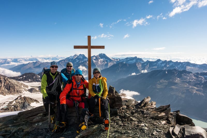 Eine Hochtourengruppe auf dem Gipfel, Panorama im Hintergrund, Gipfelkreuz