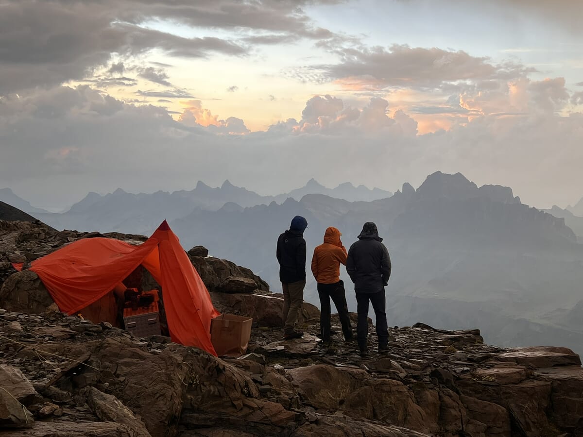 Drei Personen betrachten Berglandschaft bei Sonnenuntergang.