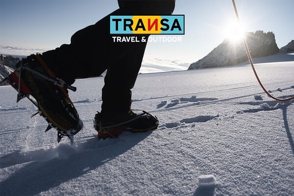 Person mit Steigeisen im Schnee bei Sonnenlicht.